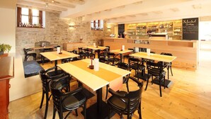 Un restaurante con mesas y sillas de madera, una pared de piedra y una zona de bar con un menú en una pizarra.