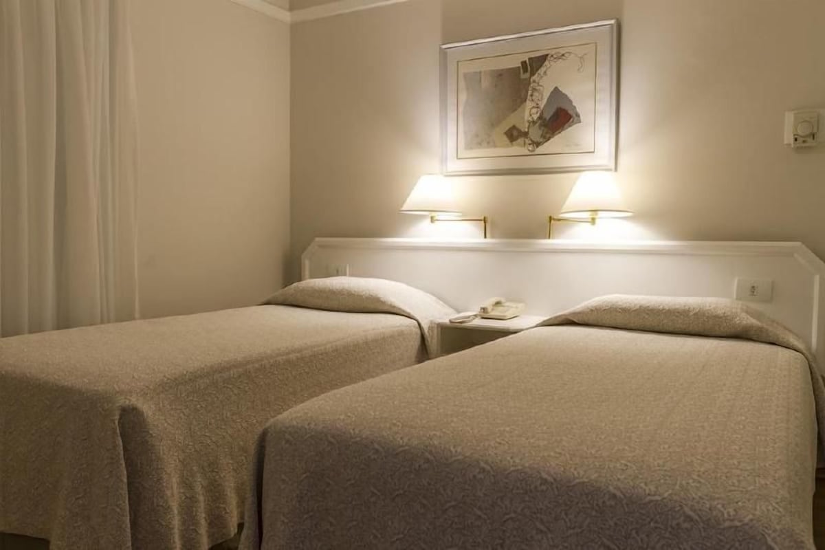 A hotel room with two beds, a nightstand, and a painting on the wall.