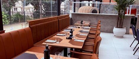 A restaurant with long wooden tables, brown leather booths, and hanging green pendant lights.