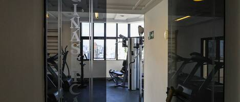 A gym with exercise equipment, large windows, and a glass door with the word 'GYNASCA' on it.