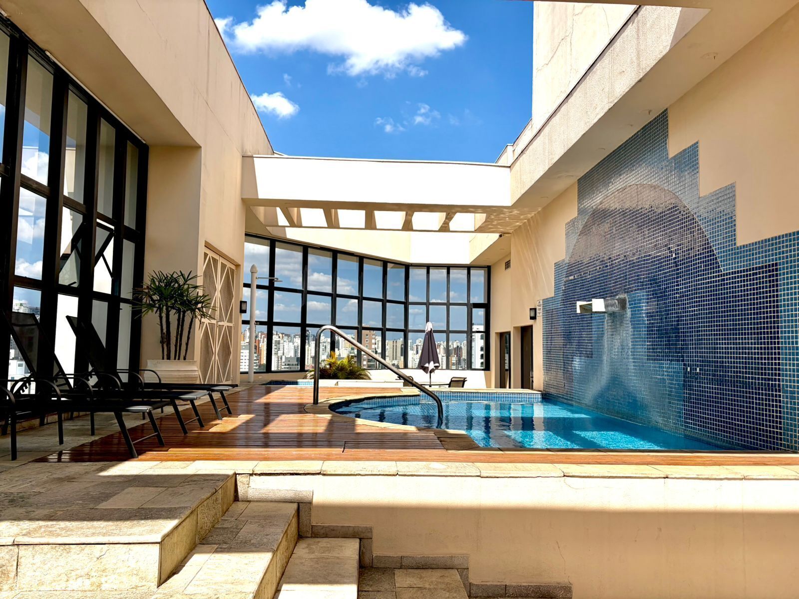 Una piscina en la azotea con vistas a la ciudad, un espacio de estar con sillas y una pared de azulejos.