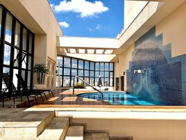 Una piscina en la azotea con vistas a la ciudad, un espacio de estar con sillas y una pared de azulejos.