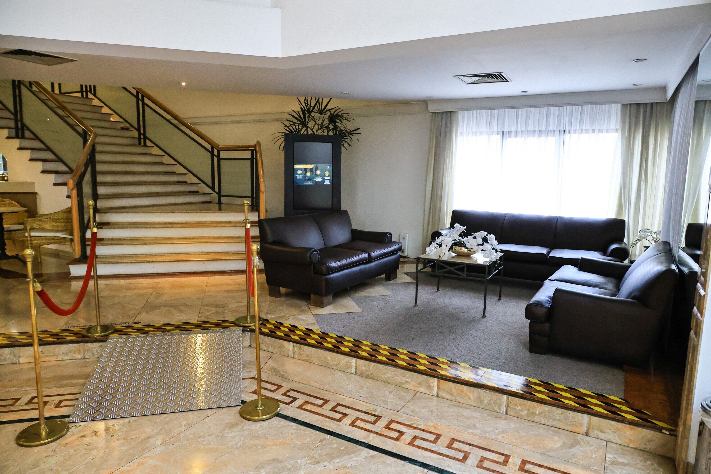 Un hall d’hôtel avec un escalier, des canapés en cuir, une table basse et un espace recouvert d’un tapis rouge.