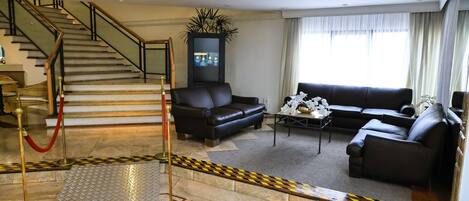 Un hall d’hôtel avec un escalier, des canapés en cuir, une table basse et un espace recouvert d’un tapis rouge.