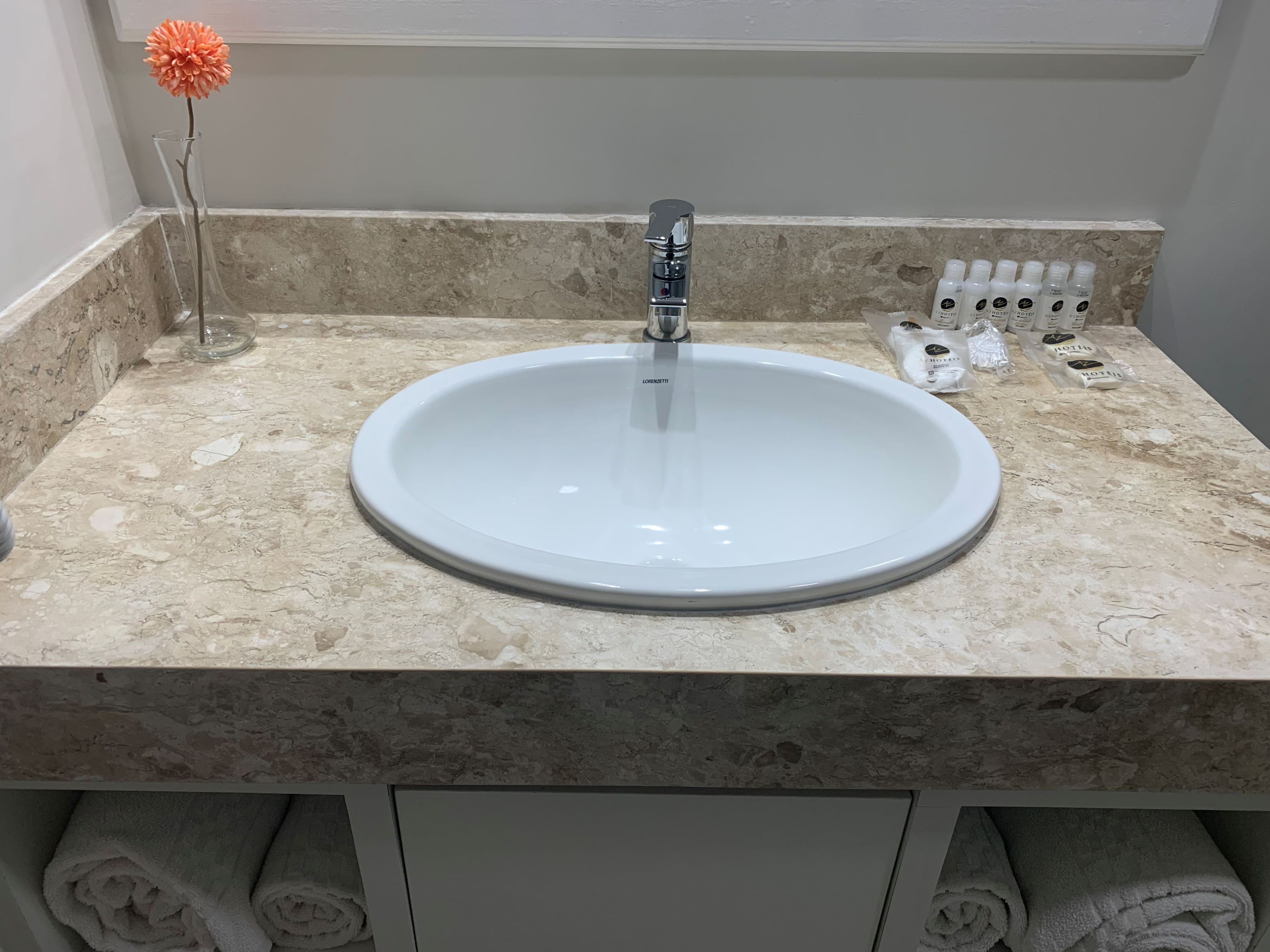 A bathroom with a white sink, a marble countertop, and a towel rack with towels.