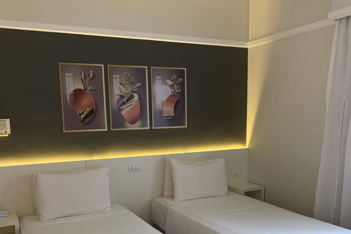 A hotel room with two beds, a nightstand, a wall-mounted light, and three framed pictures.