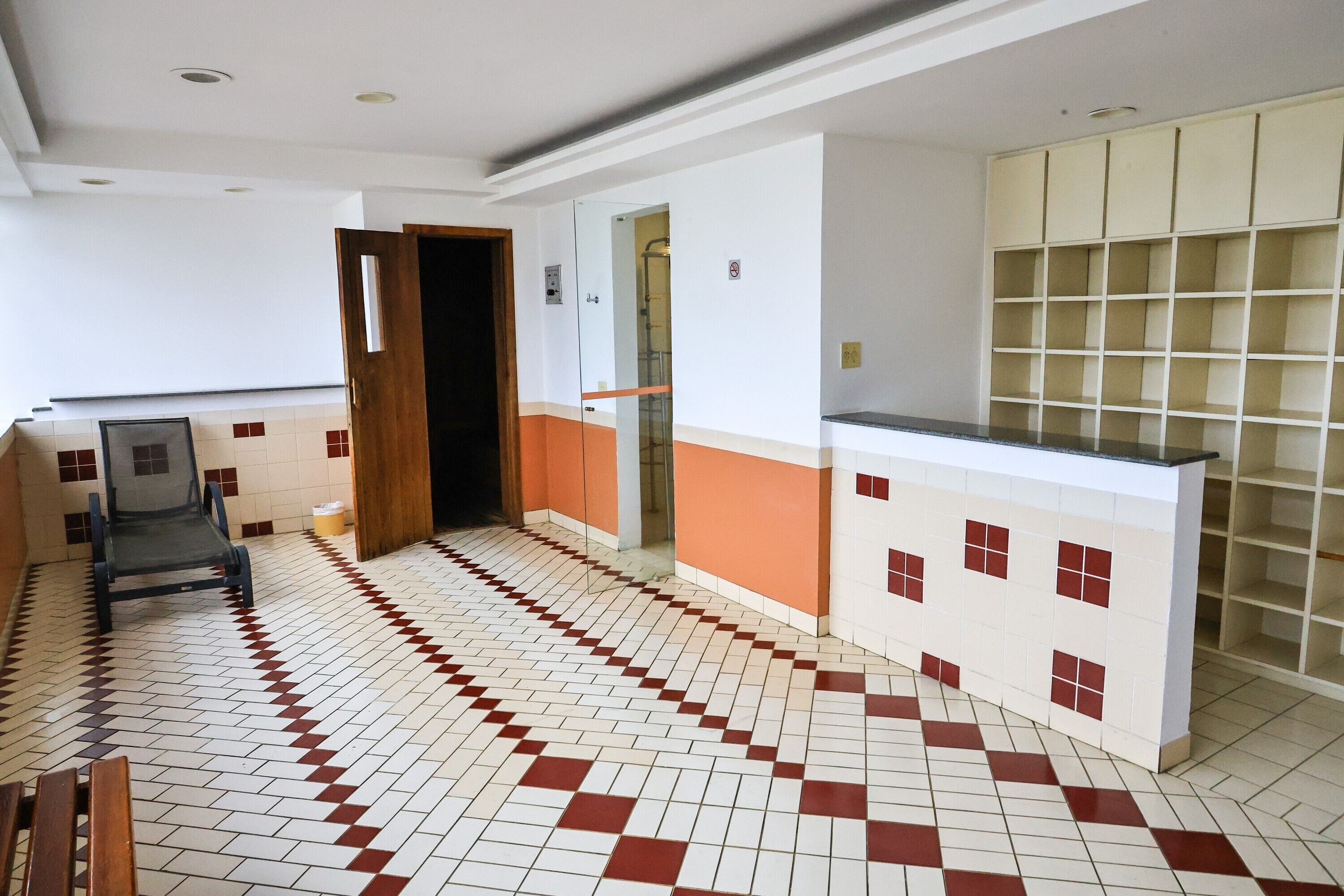 A hotel lobby with a tiled floor, a reception desk, a wooden bench, and a glass door leading to a bathroom.