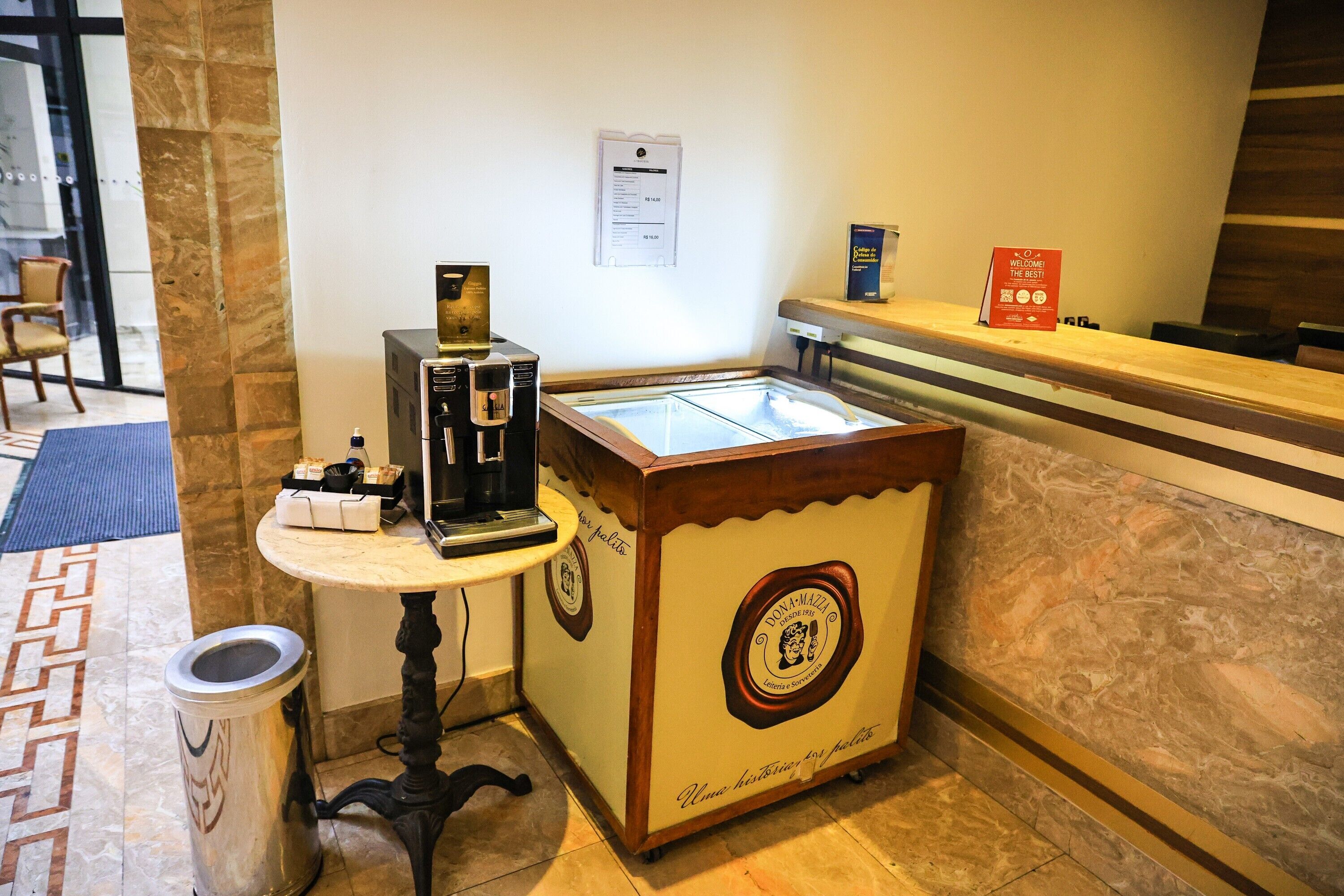 Un'area reception con una macchina da caffè, un cestino, un piccolo tavolo con il menu e un bancone con un cartello.