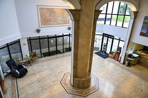 Eine Lobby mit einer großen Säule, einem Massagesessel, einem Empfangsbereich und Blick durch große Fenster.