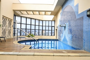 Ein Hallenbad mit Blick auf die Stadt, einer Holzterrasse und einem großen Fenster.