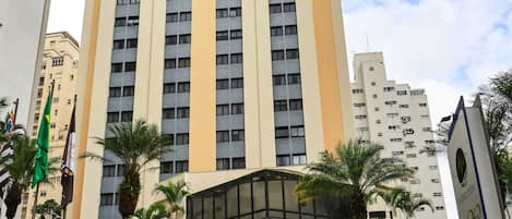 A tall building with multiple floors, a central entrance, and a surrounding grassy area with palm trees.