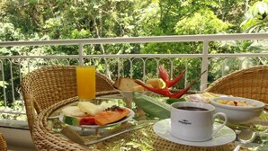 A breakfast setup on a balcony with wicker chairs, a glass table, and a view of lush greenery. - Bombinhas Summer Beach Hotel & Spa (Bombinhas)