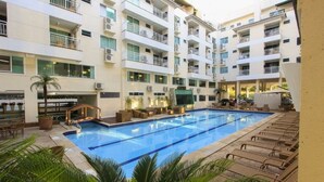 A hotel with a central swimming pool surrounded by lounge chairs and a palm tree. - Bombinhas Summer Beach Hotel & Spa (Bombinhas)