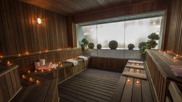 A wooden spa area with benches, candles, and a large window with a view of trees. - Bombinhas Summer Beach Hotel & Spa (Bombinhas)