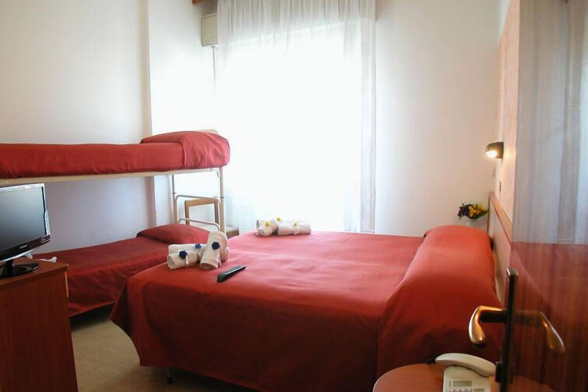 Ein Hotelzimmer mit Etagenbett, Schreibtisch inklusive Fernseher und Nachttisch mit Telefon.