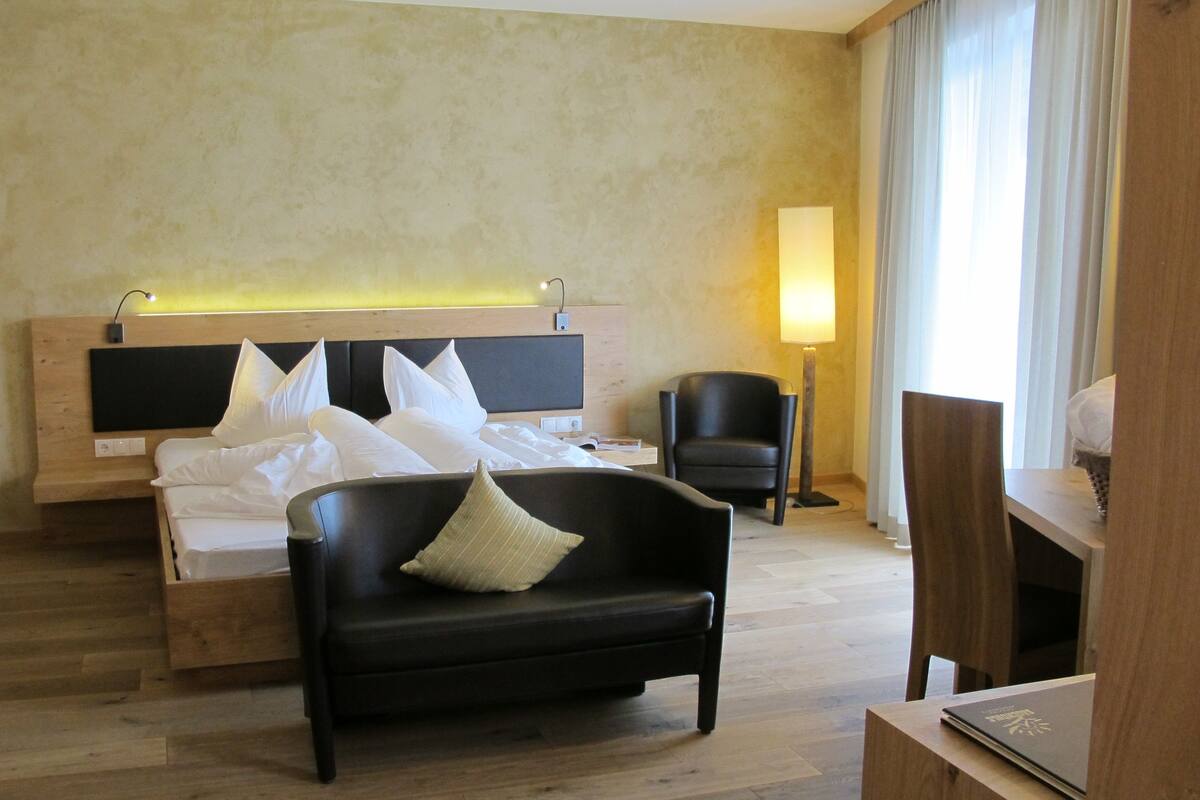 A hotel room with a bed, a black sofa, a chair, a bedside table, and a lamp.