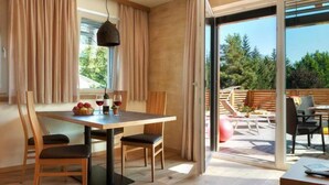 Una habitación moderna con una mesa de comedor de madera, sillas y un amplio ventanal corredera que da a un patio exterior.