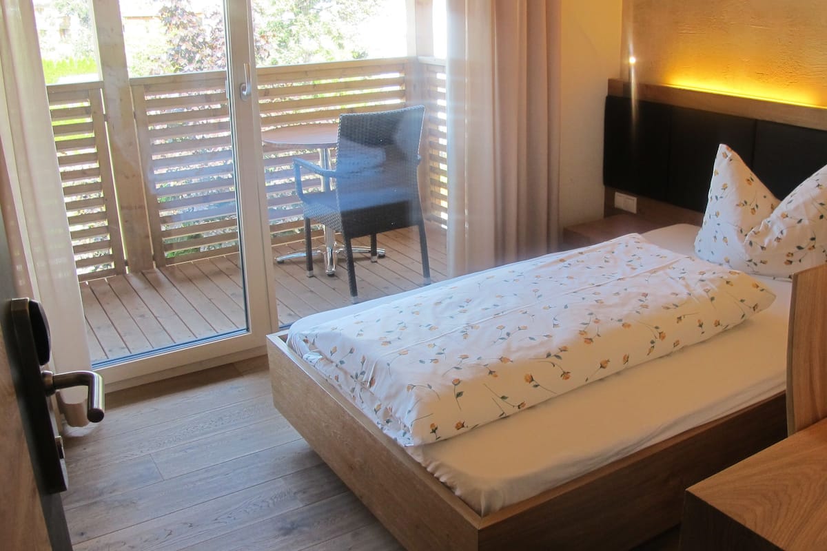 A bedroom with a wooden bed, a nightstand, and a view of an outdoor patio with a table and chairs.