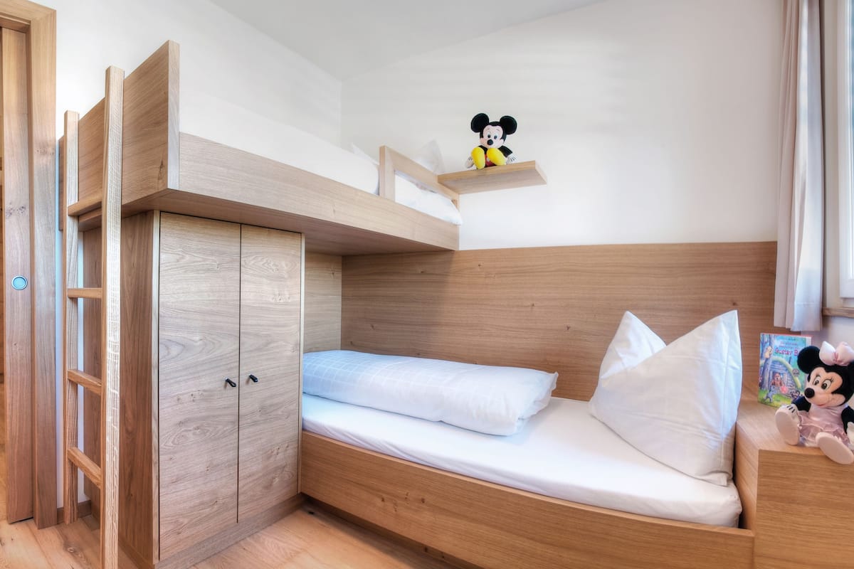 A bunk bed with a wooden headboard, a small shelf above the bed, and a Mickey Mouse figurine on the shelf.