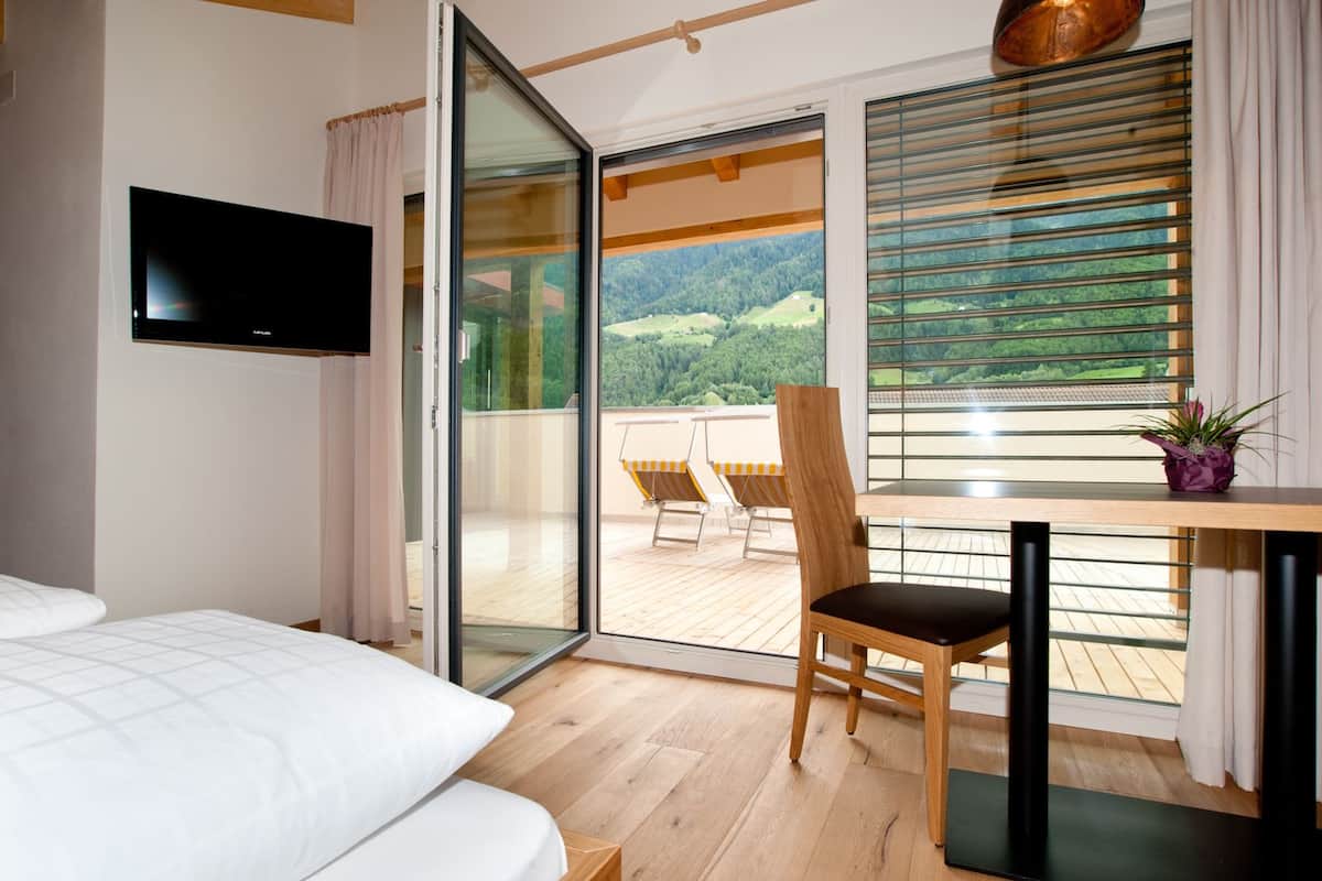 A hotel room with a bed, a TV, a balcony with a table and chairs, and a view of the outdoors.