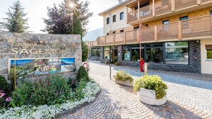 Un edificio moderno con un cartel de piedra para Camping & Residence Sagemühle, que cuenta con un acceso pavimentado y plantas en macetas.