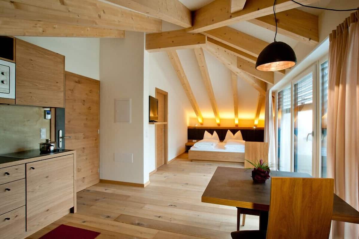 A modern bedroom with a wooden ceiling, a bed with white bedding, a bedside table, and a window with curtains.