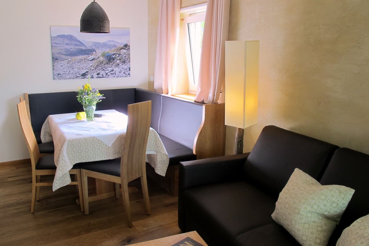 A room with a dining table, chairs, a sofa, a lamp, and a window with curtains.