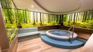 Un moderno espacio de spa con hidromasaje, suelo de madera y un mural con motivos forestales en las paredes.