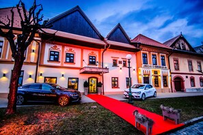 Un hotel con una alfombra roja que conduce a la entrada, un coche Renault Talisman estacionado al frente, y otro coche blanco a su lado.