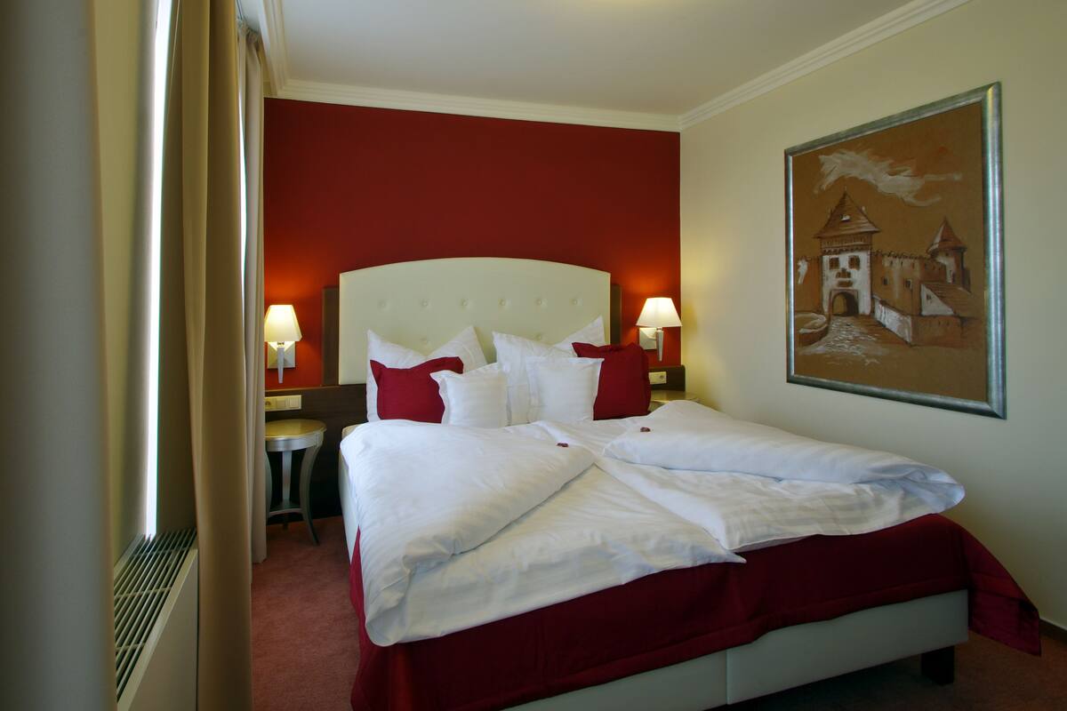 Una habitación de hotel con una cama grande, dos lámparas de noche, una pared roja y un cuadro de un castillo.