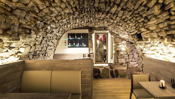 Un interior con paredes de piedra, bancos de madera y una zona de bar con botellas.