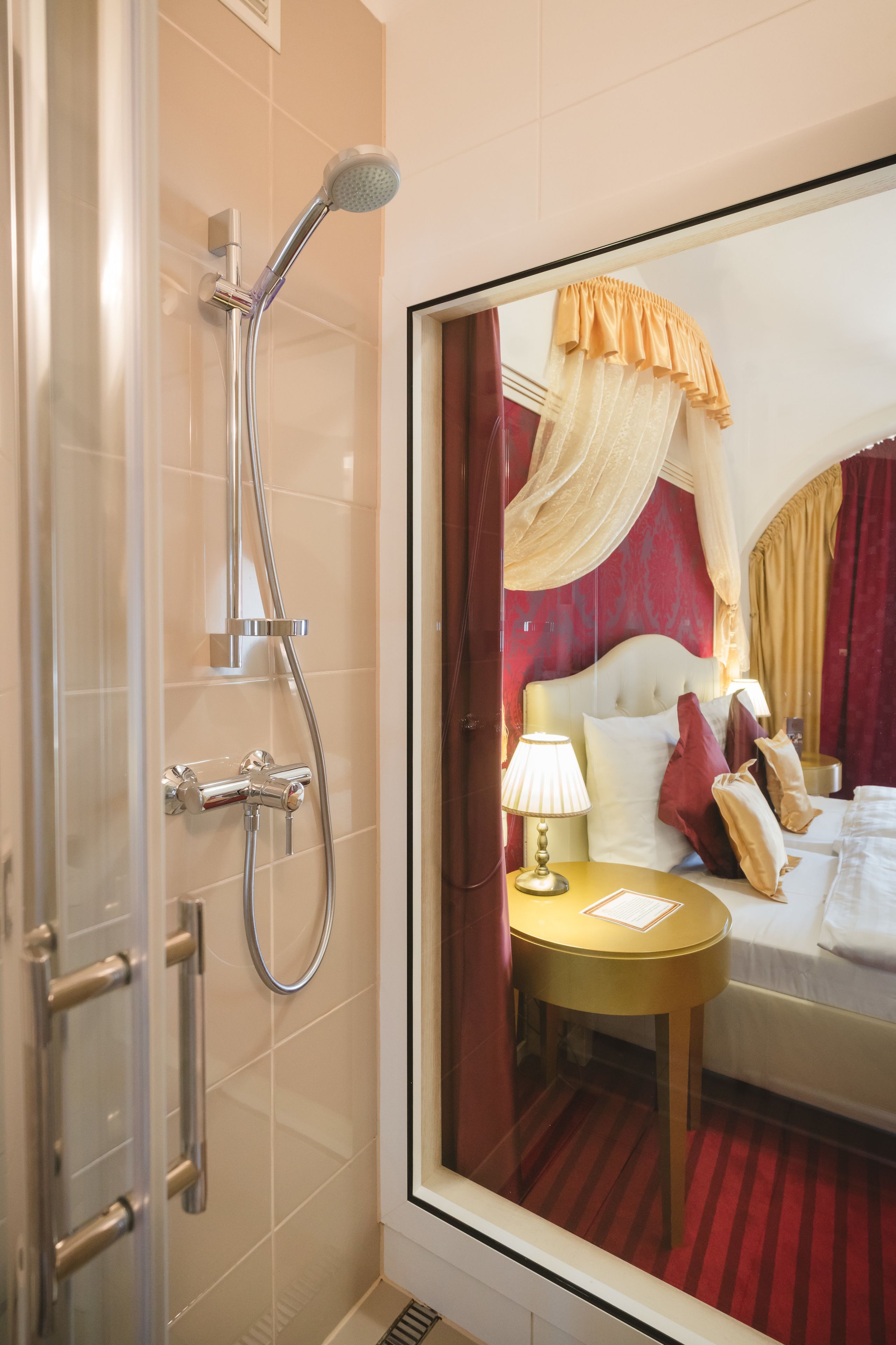 A hotel bathroom with a shower, a bed with a canopy, and a bedside table with a lamp.