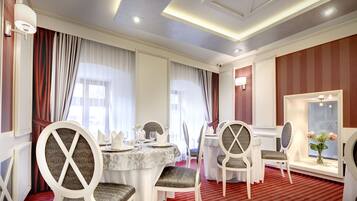 A dining area with round tables, white chairs, and a red carpet.
