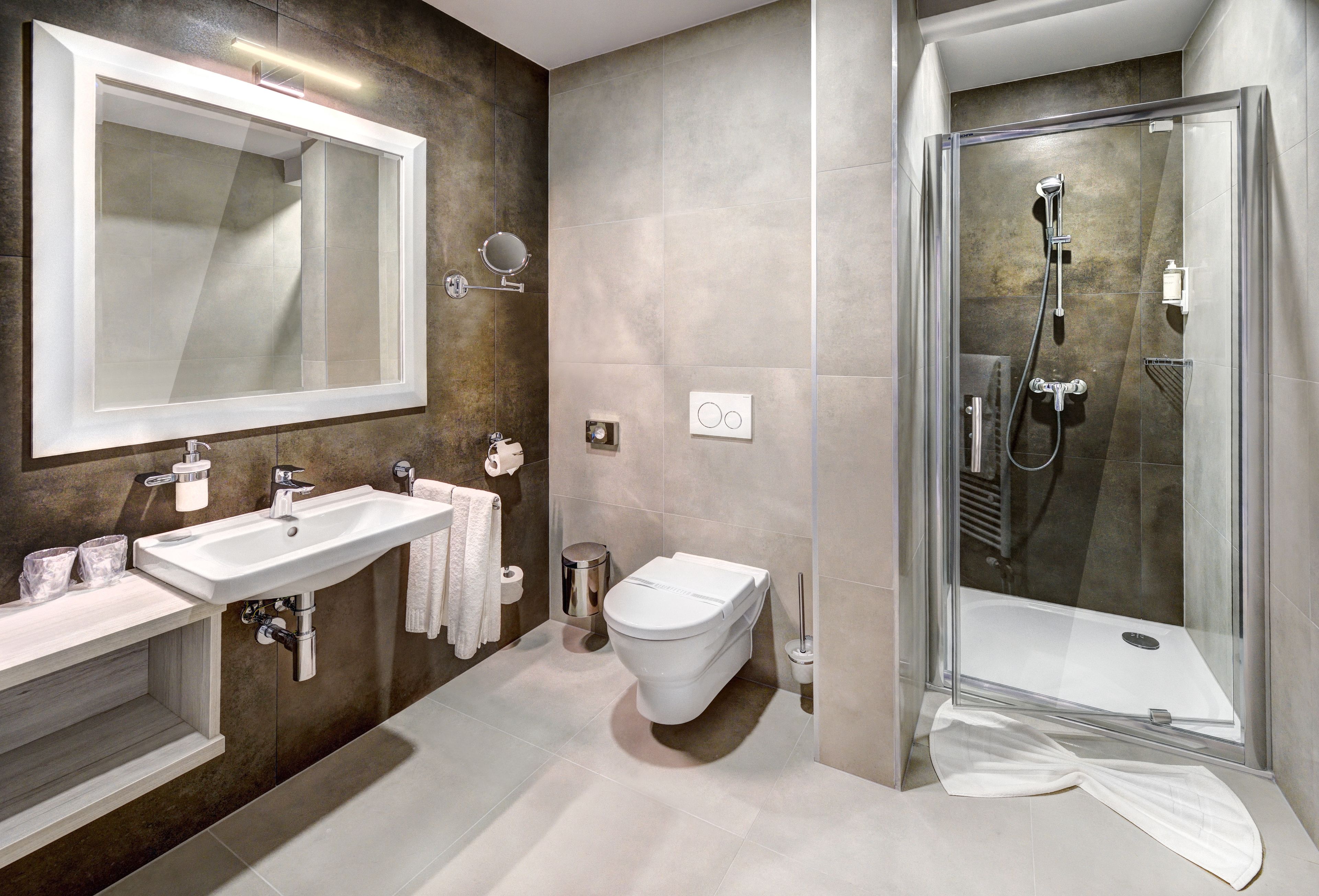 Une salle de bain moderne avec un grand miroir, deux lavabos, des toilettes et une douche à parois de verre.