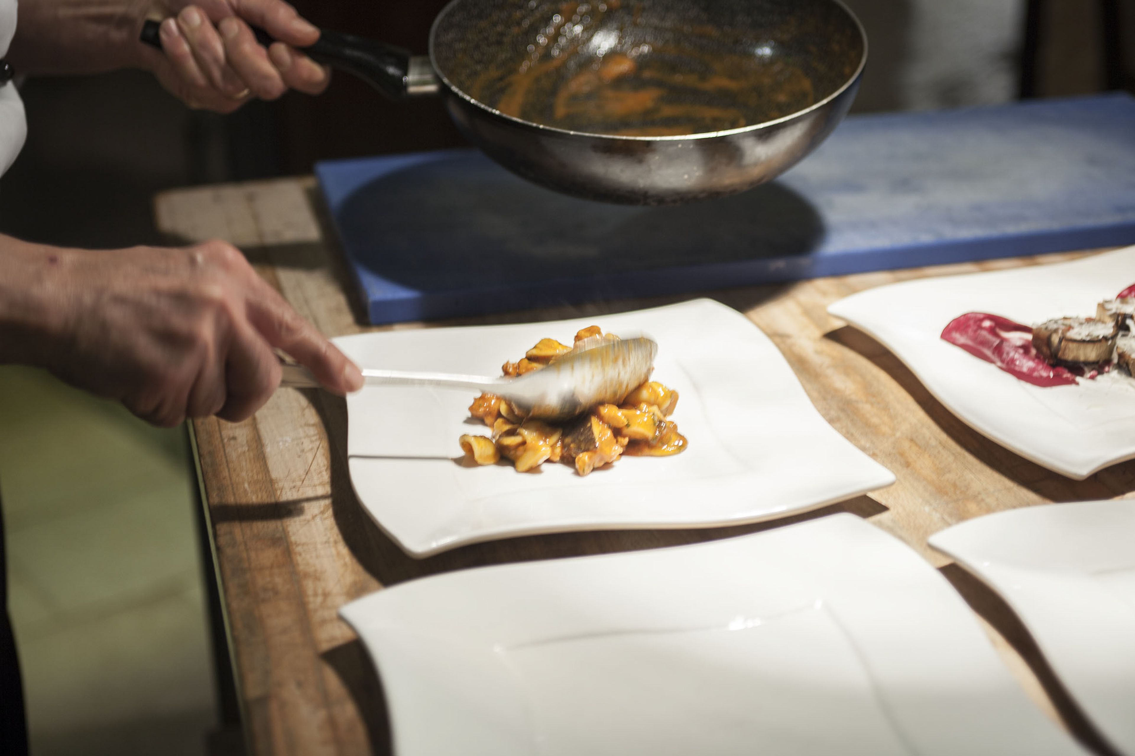 A person cooking on a wooden table with a pan and a white plate with food.