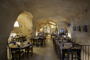 Un restaurante con mesas dispuestas para comer, una cocina al fondo y una pared de piedra rústica.