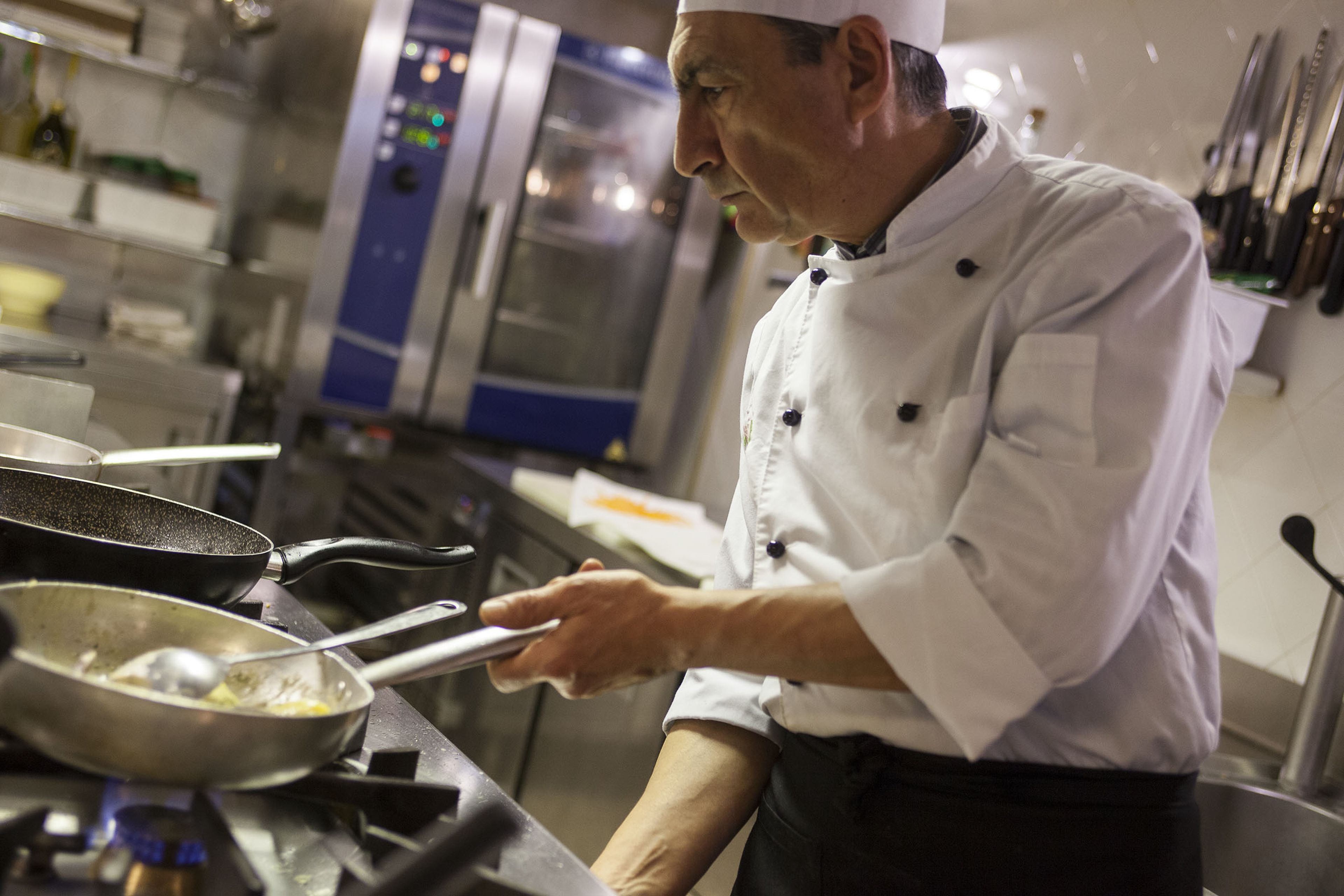 A chef in a professional kitchen with stainless steel appliances and utensils.