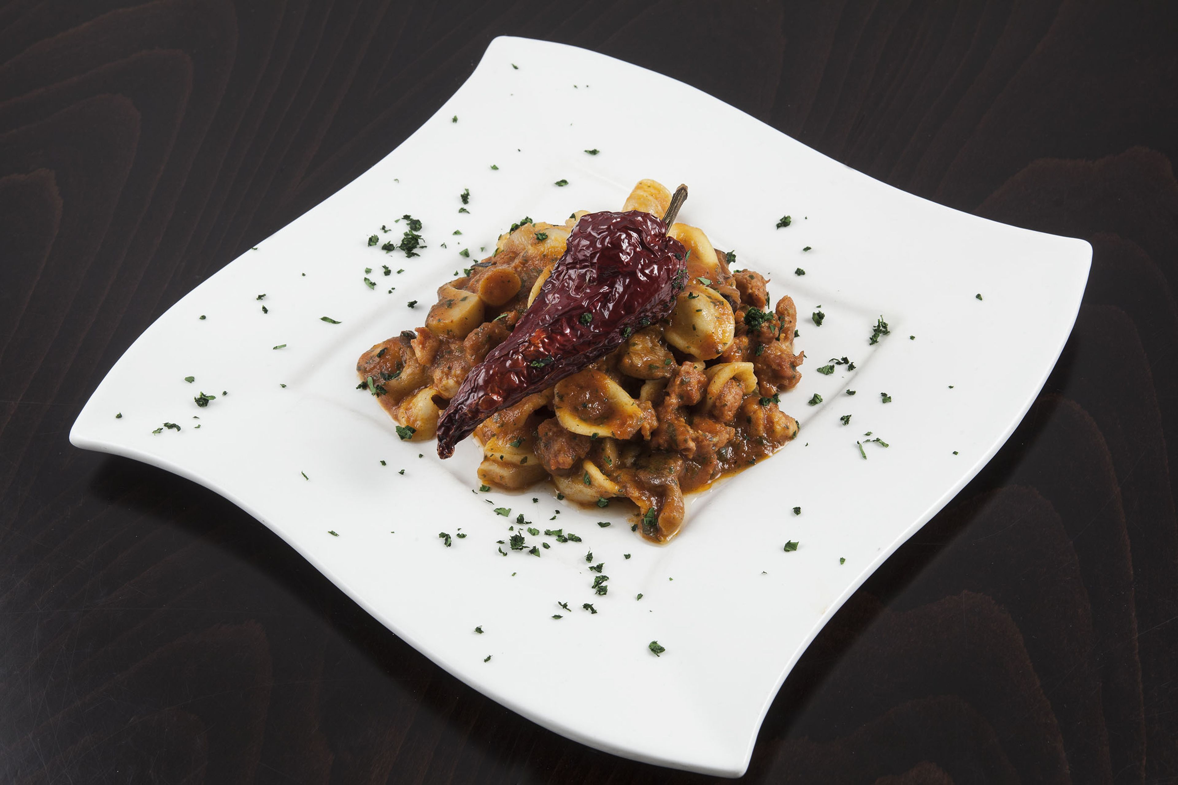 Un plato blanco con una porción de pasta, decorada con hierbas y un chile seco.
