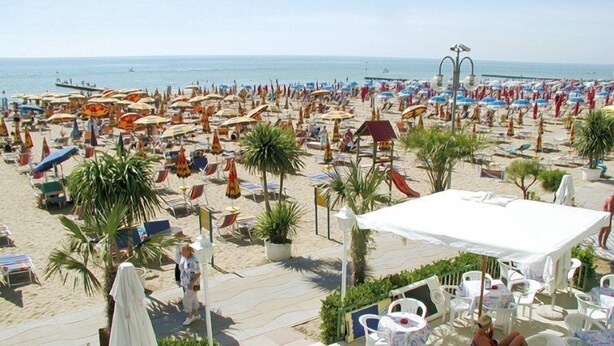 A beachside restaurant with outdoor seating, palm trees, and a view of the beach and sea. - Hotel Solemare (Jesolo)