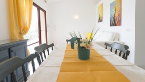 Un comedor con una mesa dispuesta para cuatro personas, un jarrón de flores y dos cuadros en la pared.