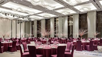 A banquet hall with round tables, purple chairs, and a high ceiling with modern lighting fixtures.