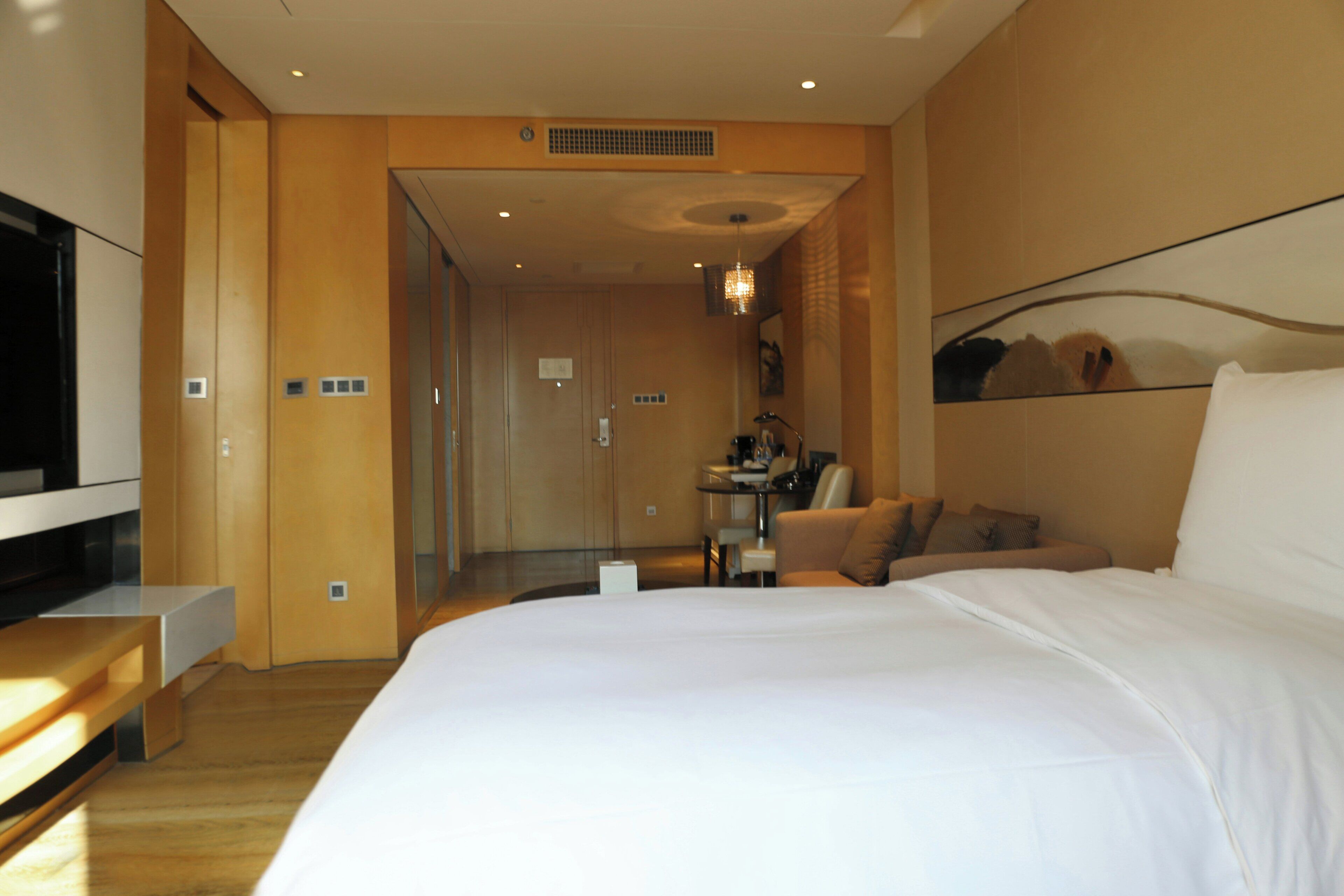 A hotel room with a large bed, a desk, a chair, a TV, and a mirror.