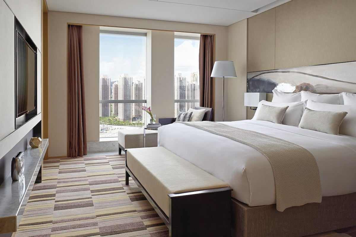 Une chambre d’hôtel moderne dotée d’un grand lit, d’un téléviseur à écran plat, d’un banc et offrant une vue sur le paysage urbain.