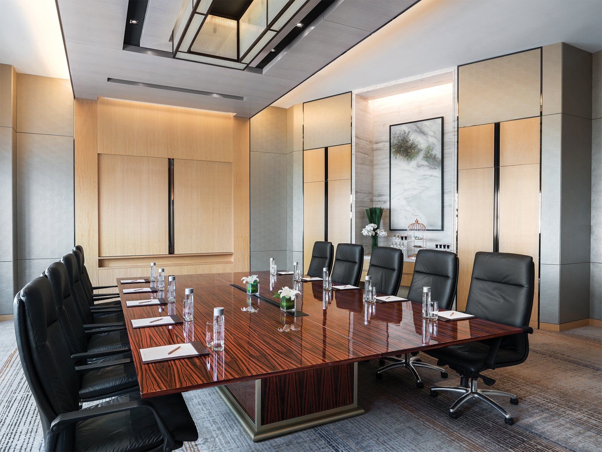 Une salle de conférence avec une longue table en bois, des fauteuils en cuir noir et un grand tableau accroché au mur.