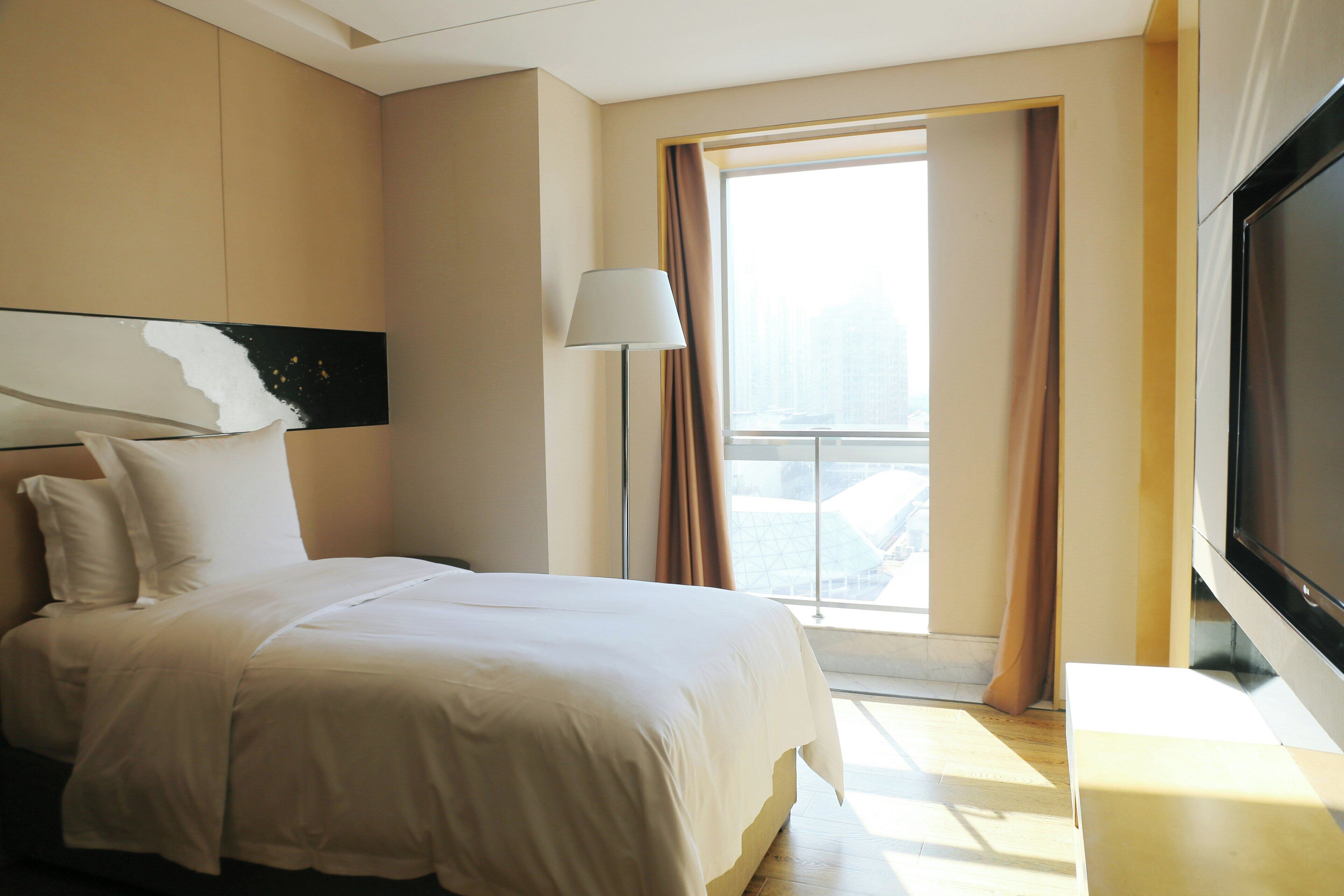 Hotelkamer met een groot bed, een flatscreen televisie, een raam met gordijnen en uitzicht op de stad.