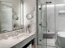 Un baño moderno con tocador de mármol, dos espejos redondos, ducha con mampara de vidrio y bañera blanca.