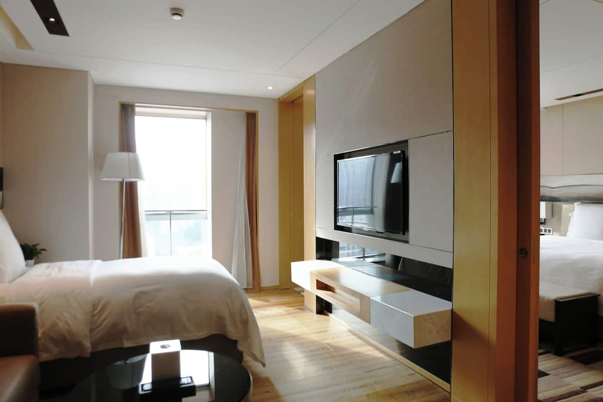 Une chambre d’hôtel moderne dotée d’un grand lit, d’un téléviseur à écran plat fixé au mur, d’un bureau avec une lampe et d’une fenêtre avec des rideaux.