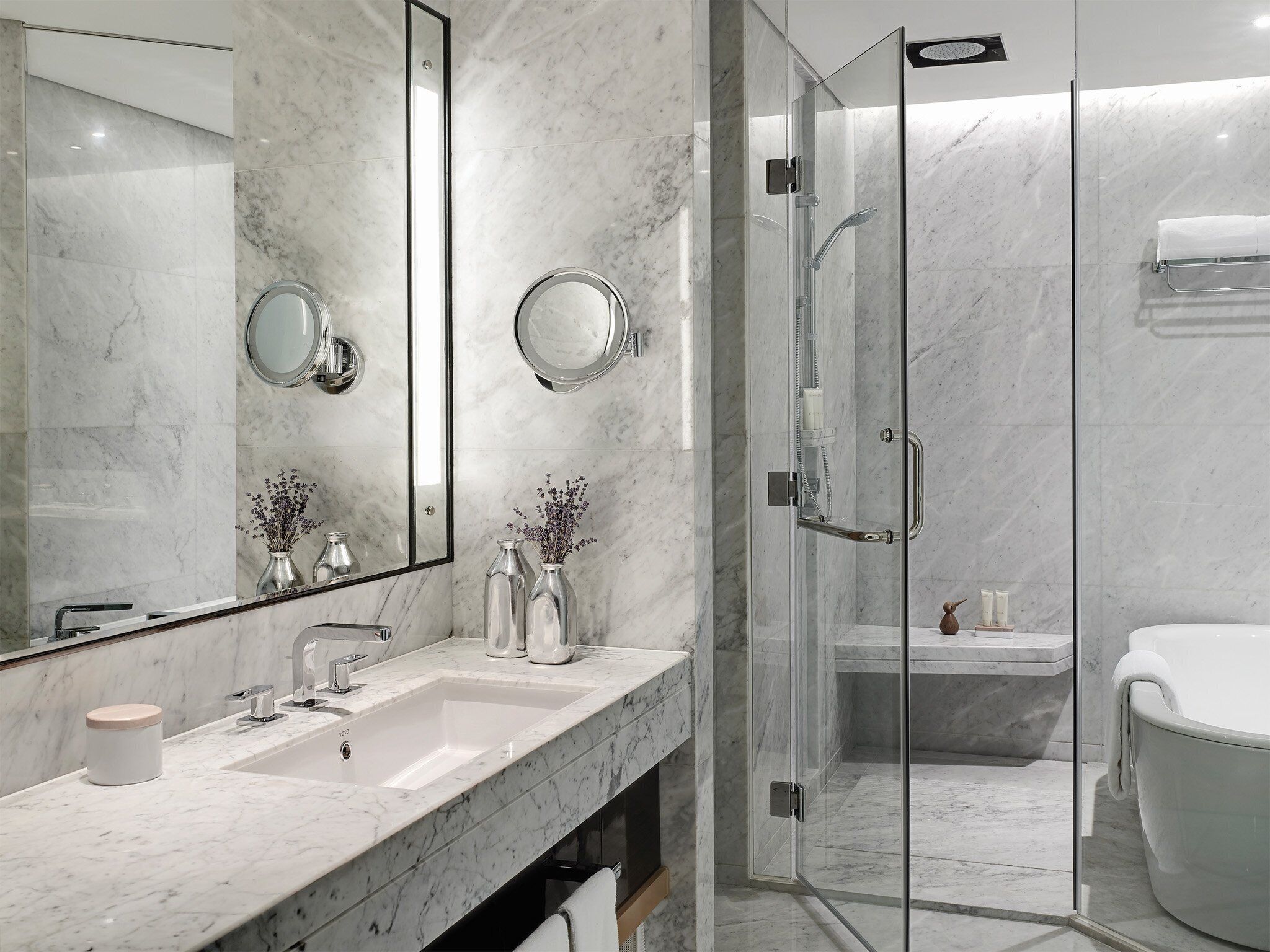A modern bathroom with a marble vanity, two sinks, a large mirror, and a glass-enclosed shower area.