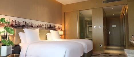 Una camera d'albergo moderna con un letto grande, un comodino con una lampada, una pianta in vaso e un quadro con una vista sulla città.