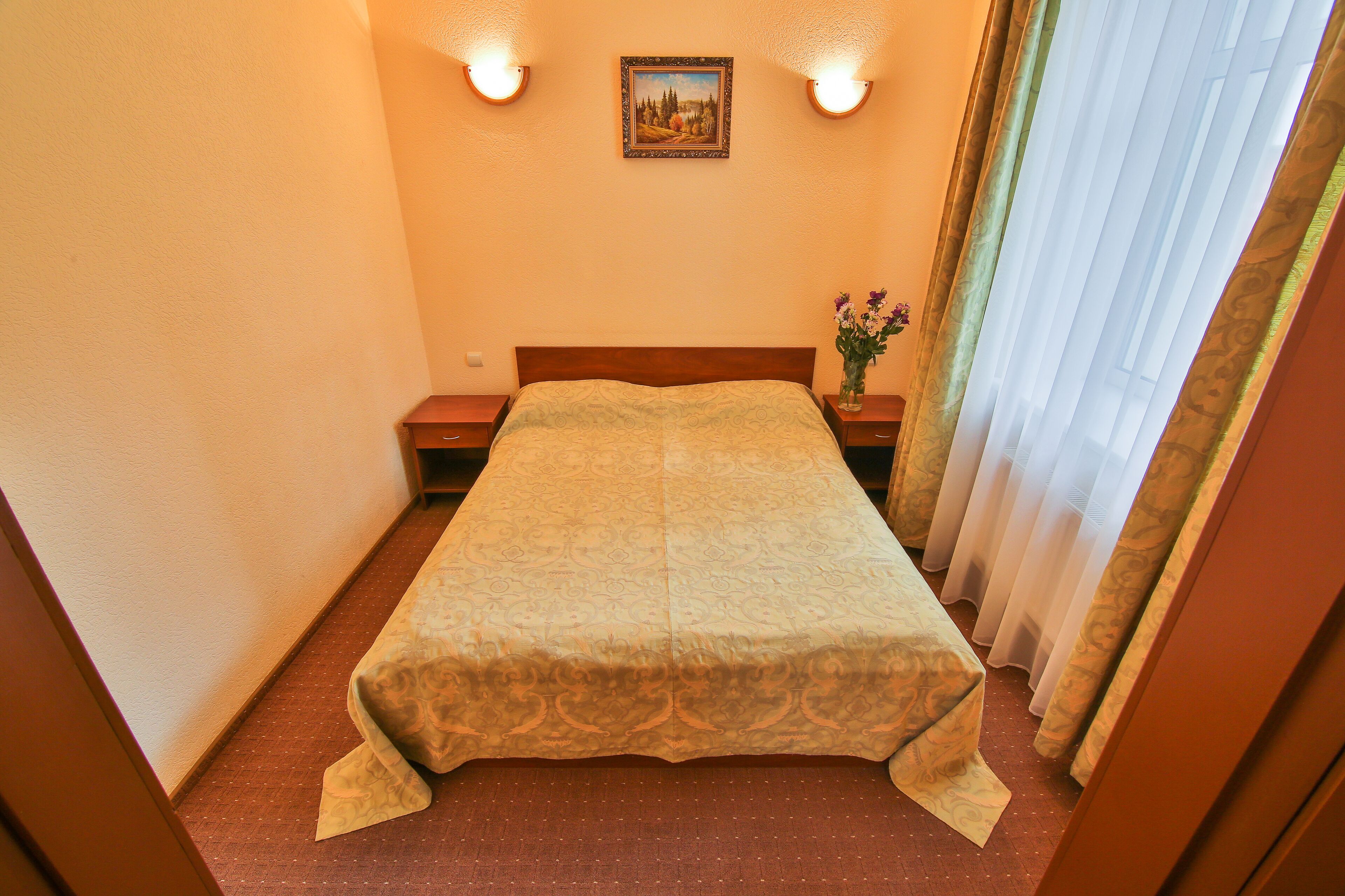 A hotel room with a bed, a nightstand, a lamp, and a painting on the wall.